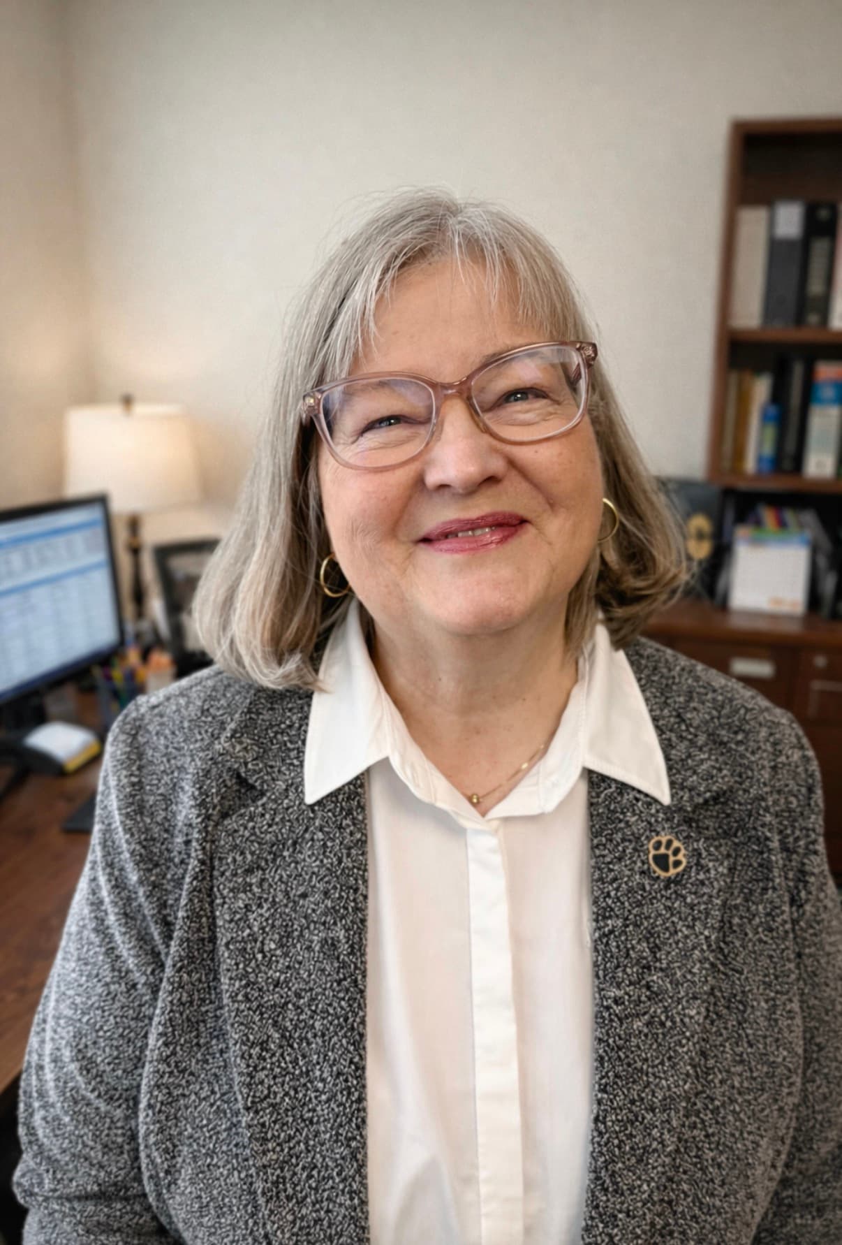 Smiling woman with gray hair and glasses, wearing a gray blazer in her office.