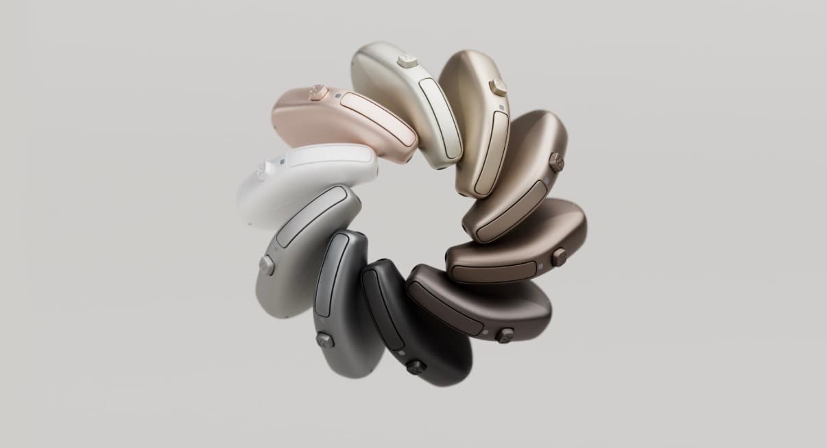 Various metallic and neutral hearing aids arranged in a circle on a grey background.