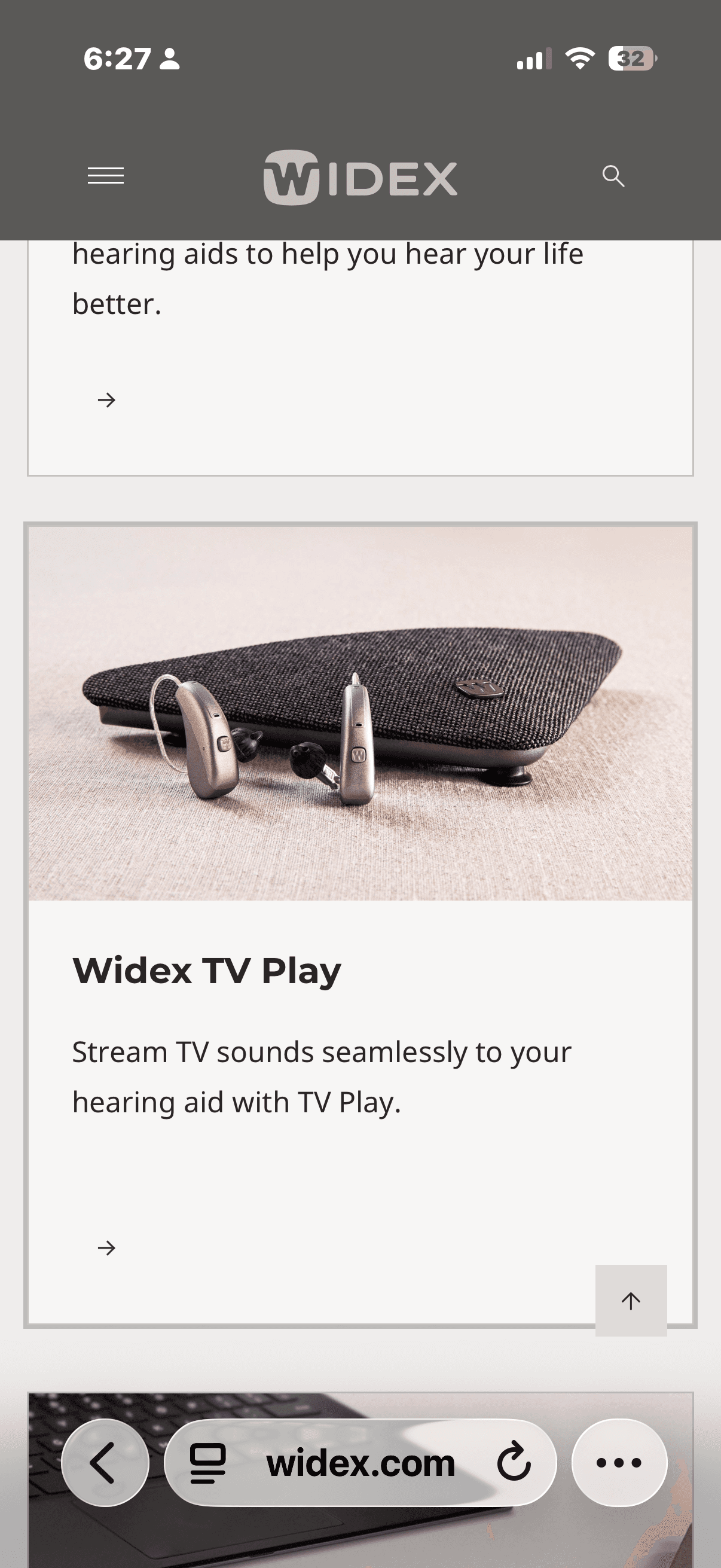 Silver hearing aids placed in front of a dark grey Widex TV Play audio transmitter.