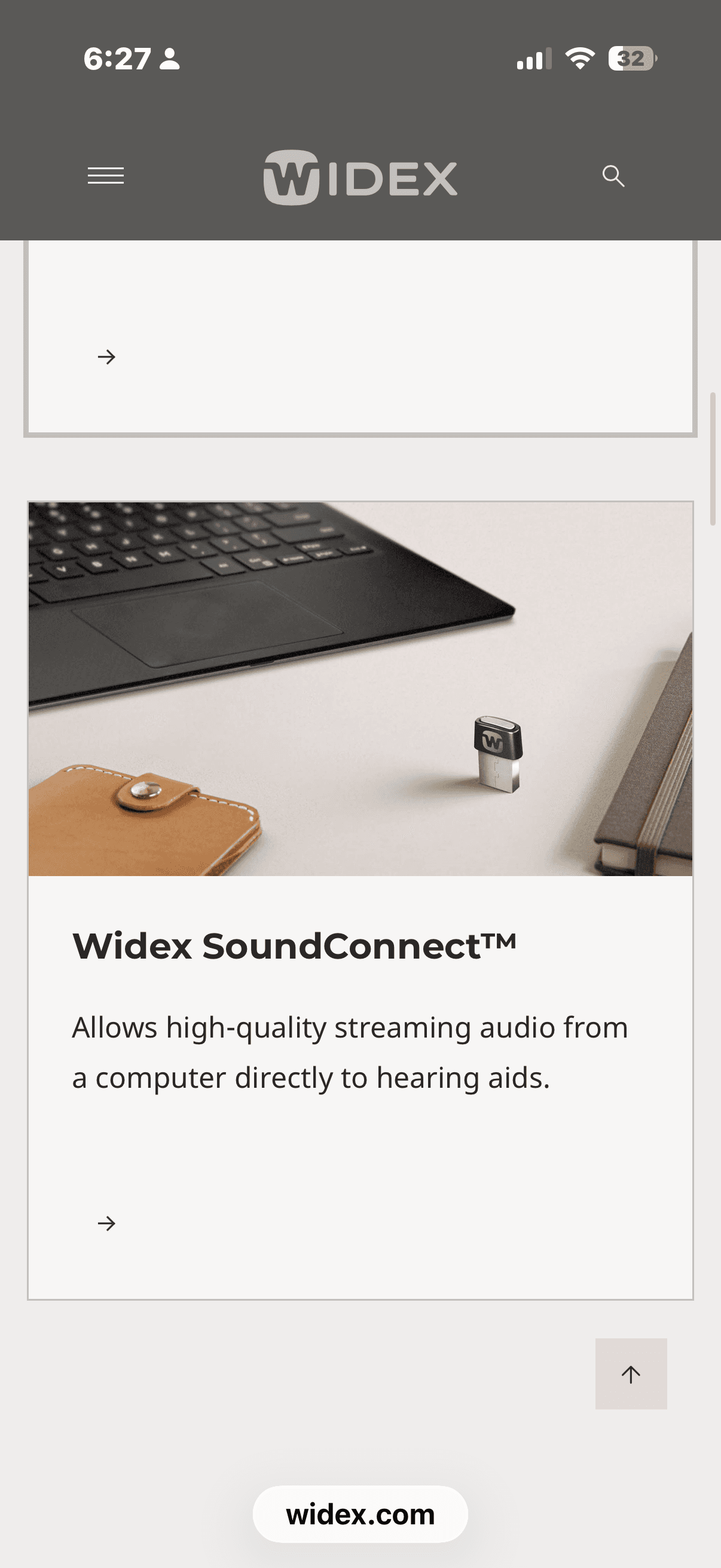 Widex SoundConnect USB dongle on a desk next to a laptop and a leather case.