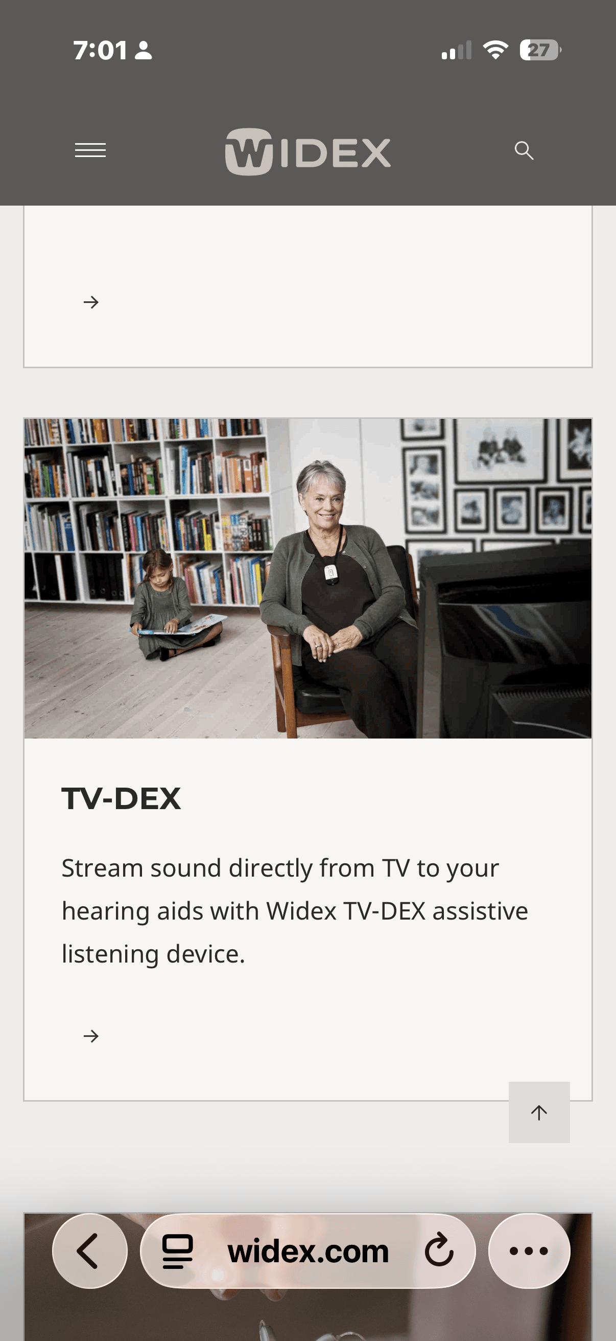Smiling woman wearing a TV-DEX device around her neck while sitting near a television.